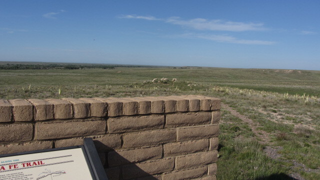 A brick wall with a wayside in front of it displaying, overlooking a wide, open landscape.