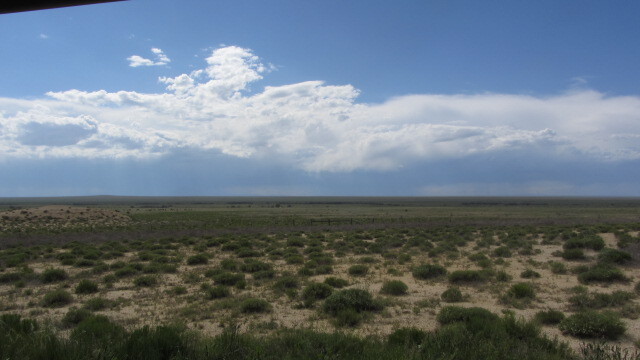A wide view of a flat, grassy landscape and a cloudy sky above.