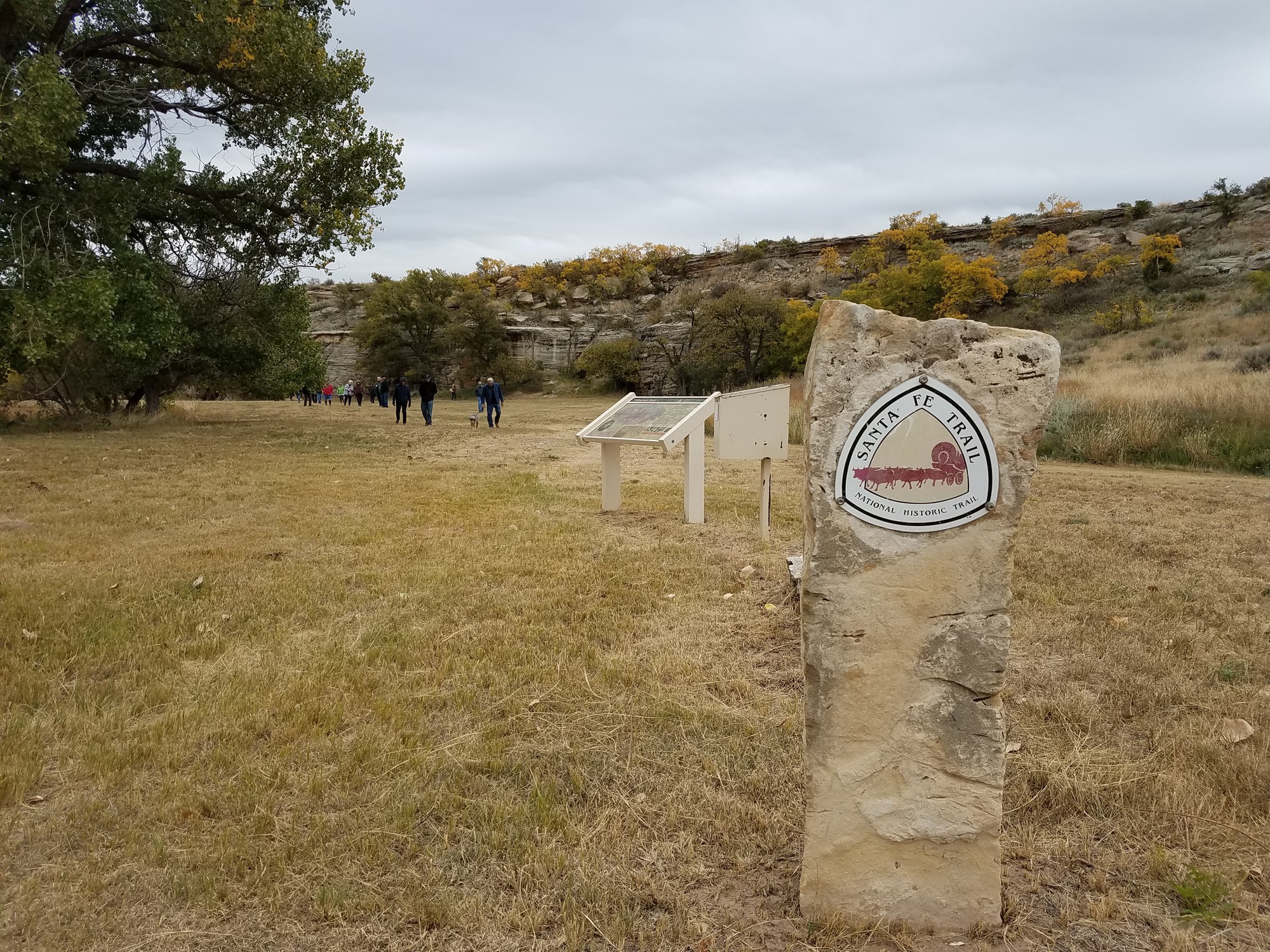 A sign with the text " Santa Fe Trail: National Historic Trail" on it in the right side of a grassy field.