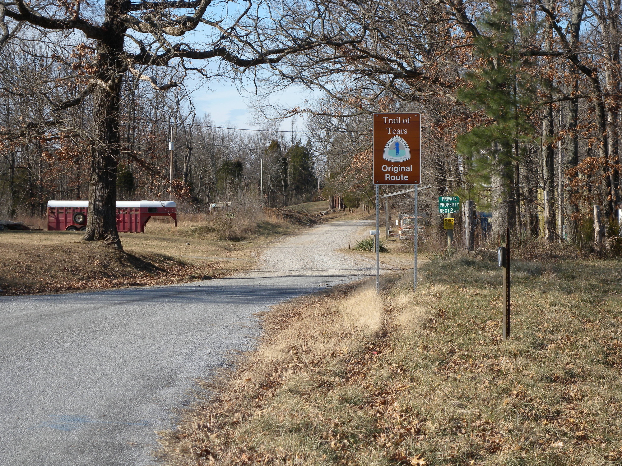 A dirt road with a sign in the middle of a wooded area.
