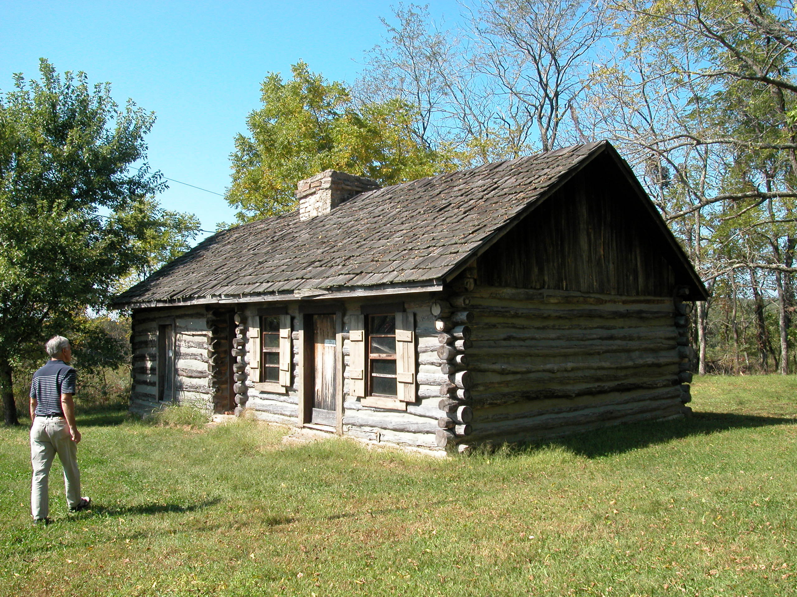 A person is standing in front of a log cabin.