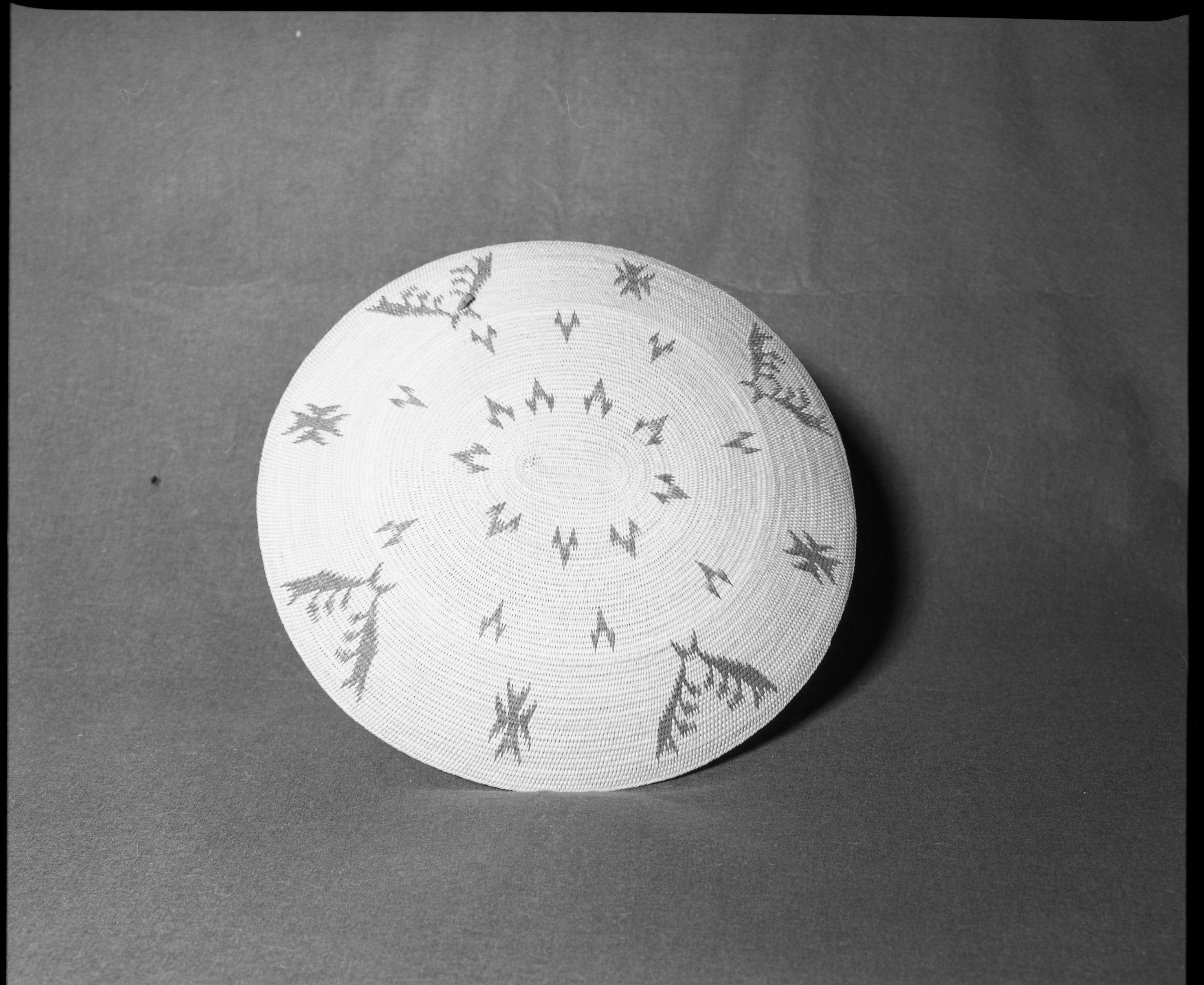 Mrs. Donald Segerstrom Collection. Object: Washoe (?) basket. Dimensions: 16 x 15 x 3". Materials: Willow, redbud, dyed and undyed fern root, pheasant neck feathers. Technology: Single rod construction, leftward coil direction, overstitched rim, moving ends bound under, fag ends concealed on back face, formerly had at least two tufts of feathers only one of which now remains intact. Photographed by Michael Dixon. Catalogued by Craig Bates and Barbara Beroza. Yosemite Collections, National Park Service. 1/83.