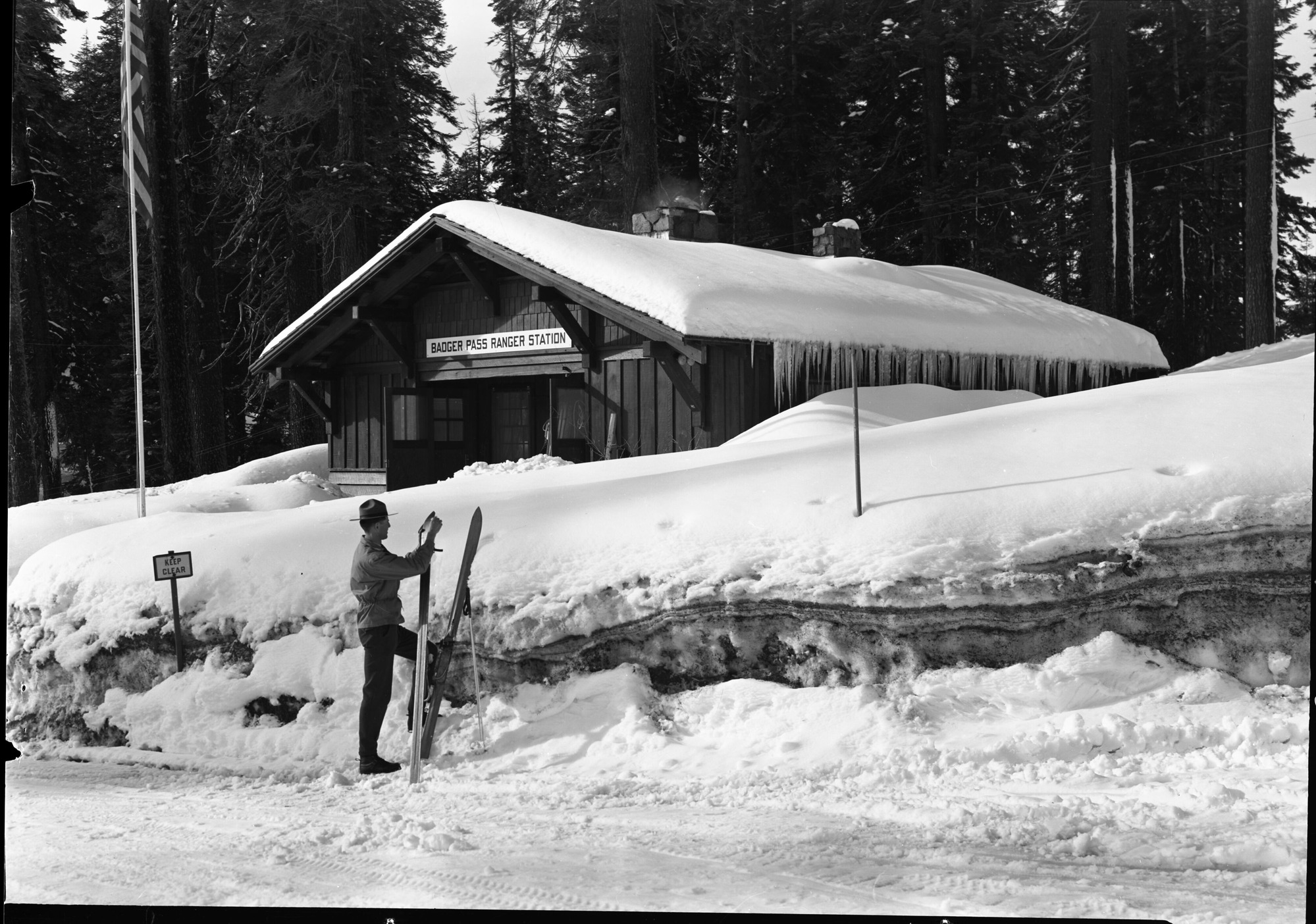 Ranger waxing skis in front of 6 ft. snow bank around Badger Pass Ranger Station.