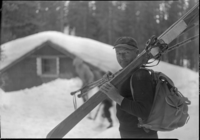 Jule Frisch, Swiss ski instructor, is shown here starting out on an all day trek into the Yosemite high country. Ski lodge almost buried in snow in background.