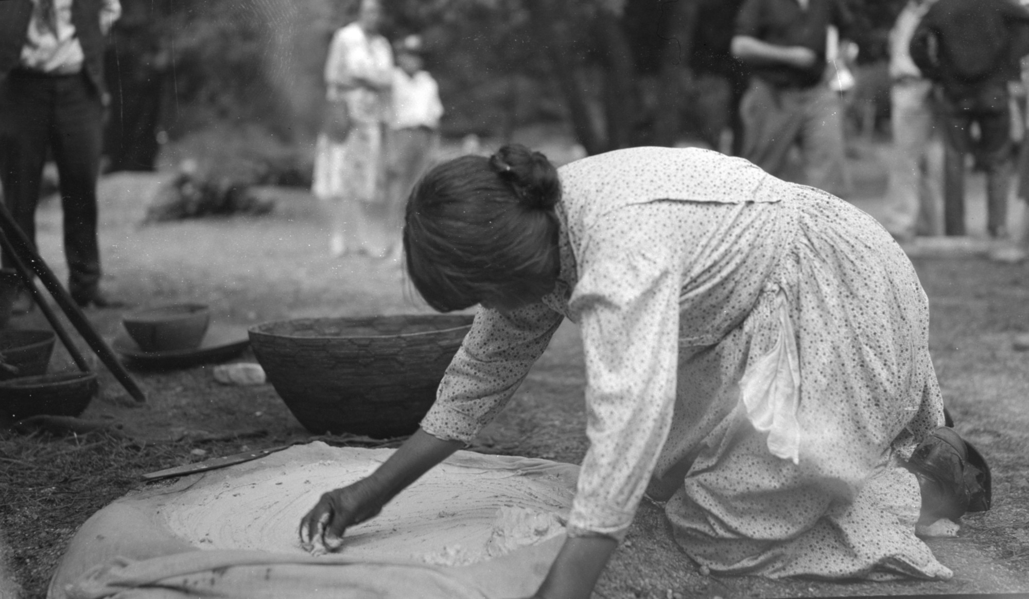 Maggie Howard picking up leached acorn dough from leaching basin--all baskets in museum.