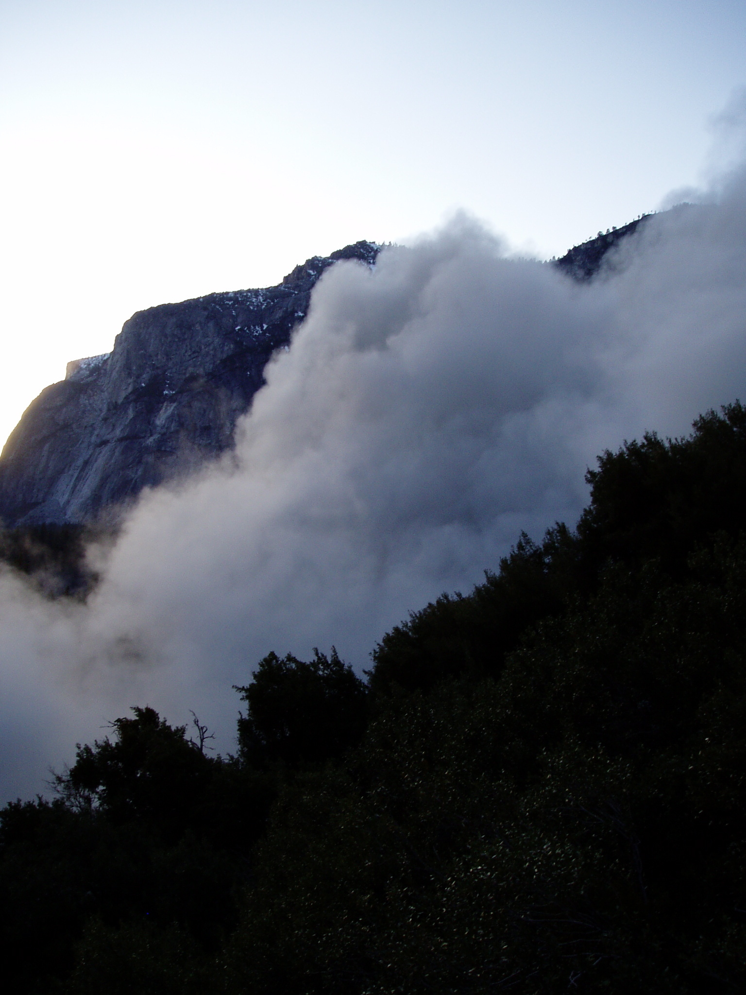 White rock fall dust cloud rising above the valley with the outline of steep rock walls on either side.
