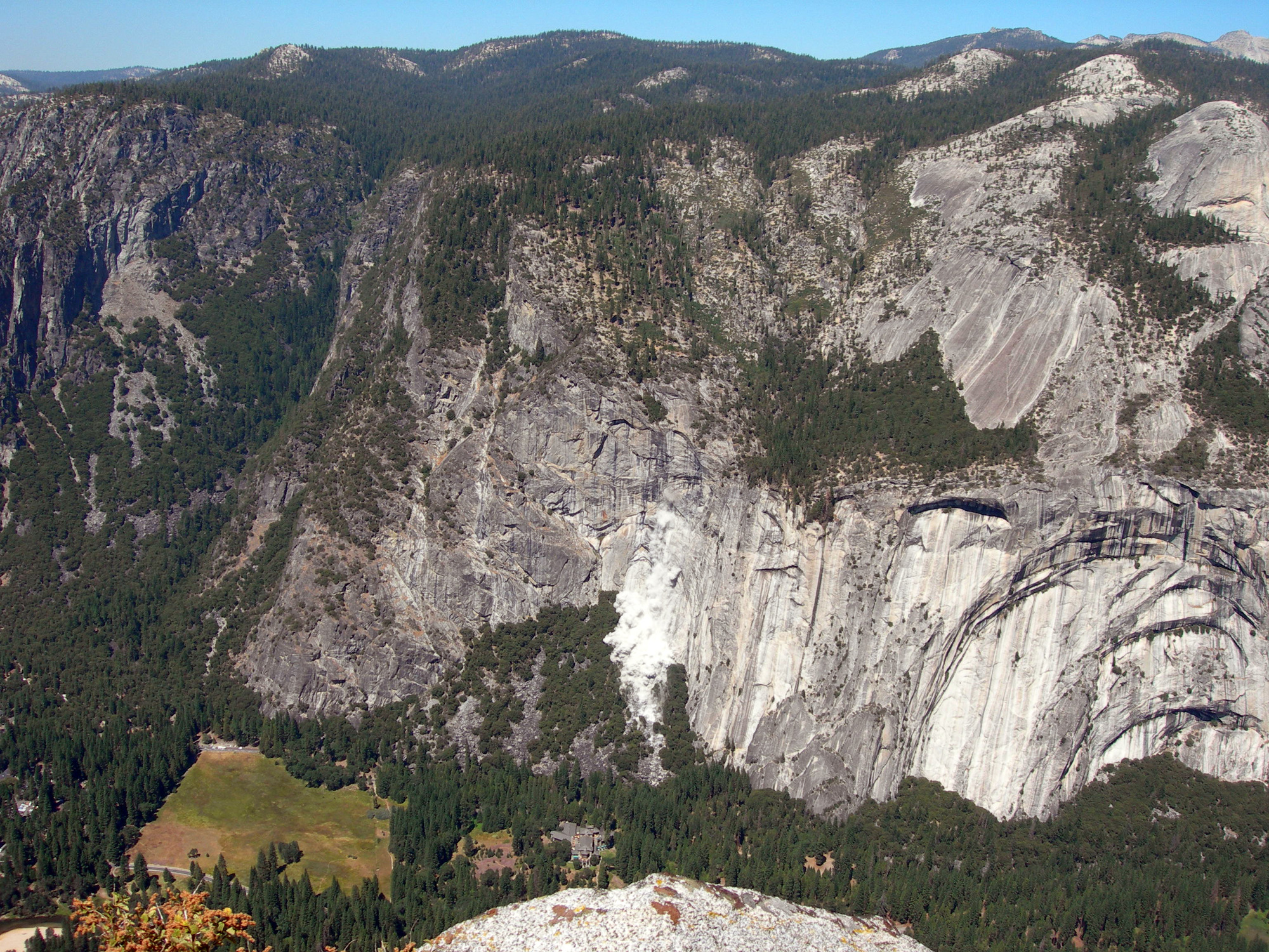 A billowing white dust cloud rises from a cliff face above a sloping talus cone.