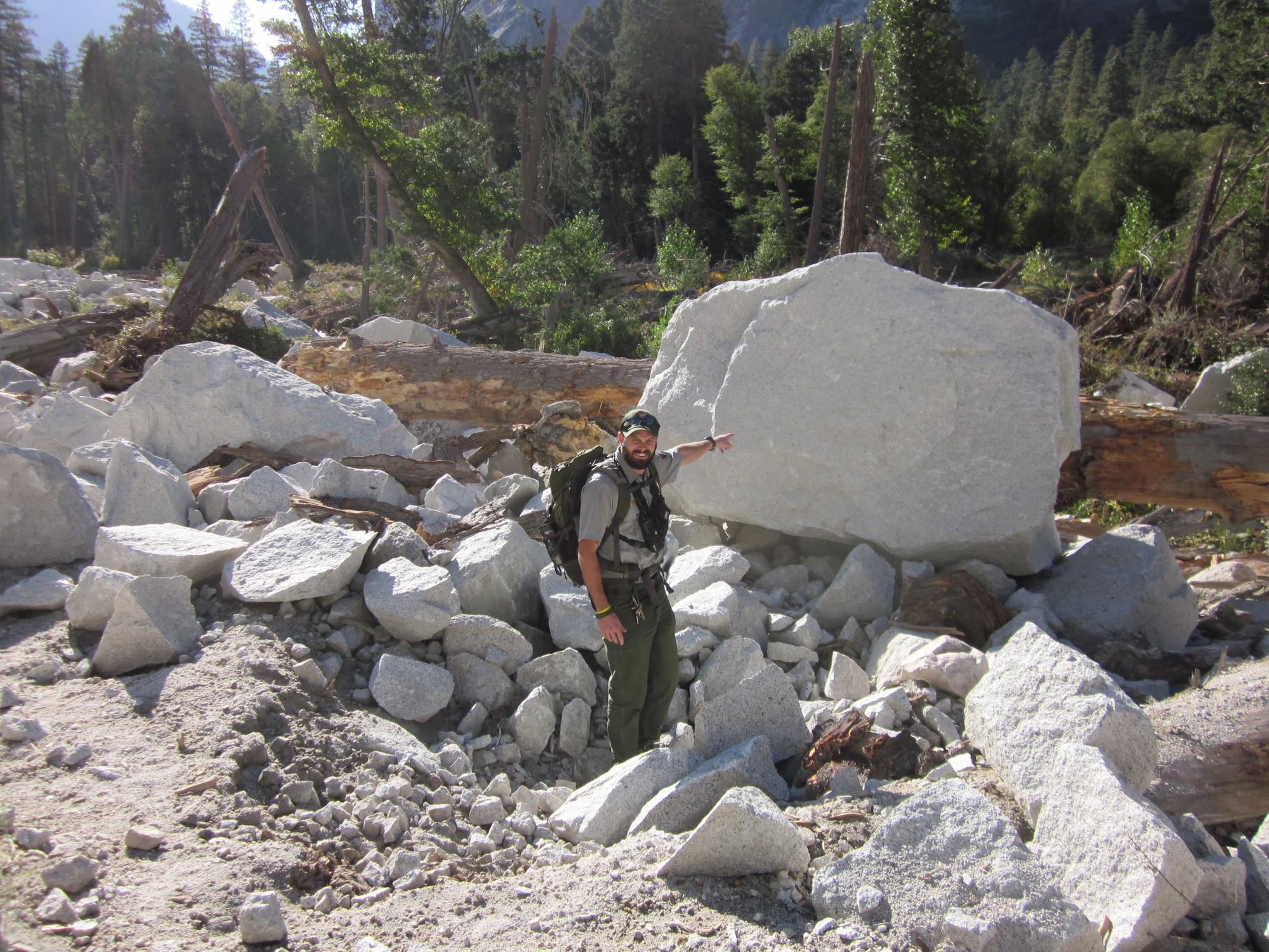 A large fresh boulder just beyond the trail. A person for scale stands next to the boulder and points.