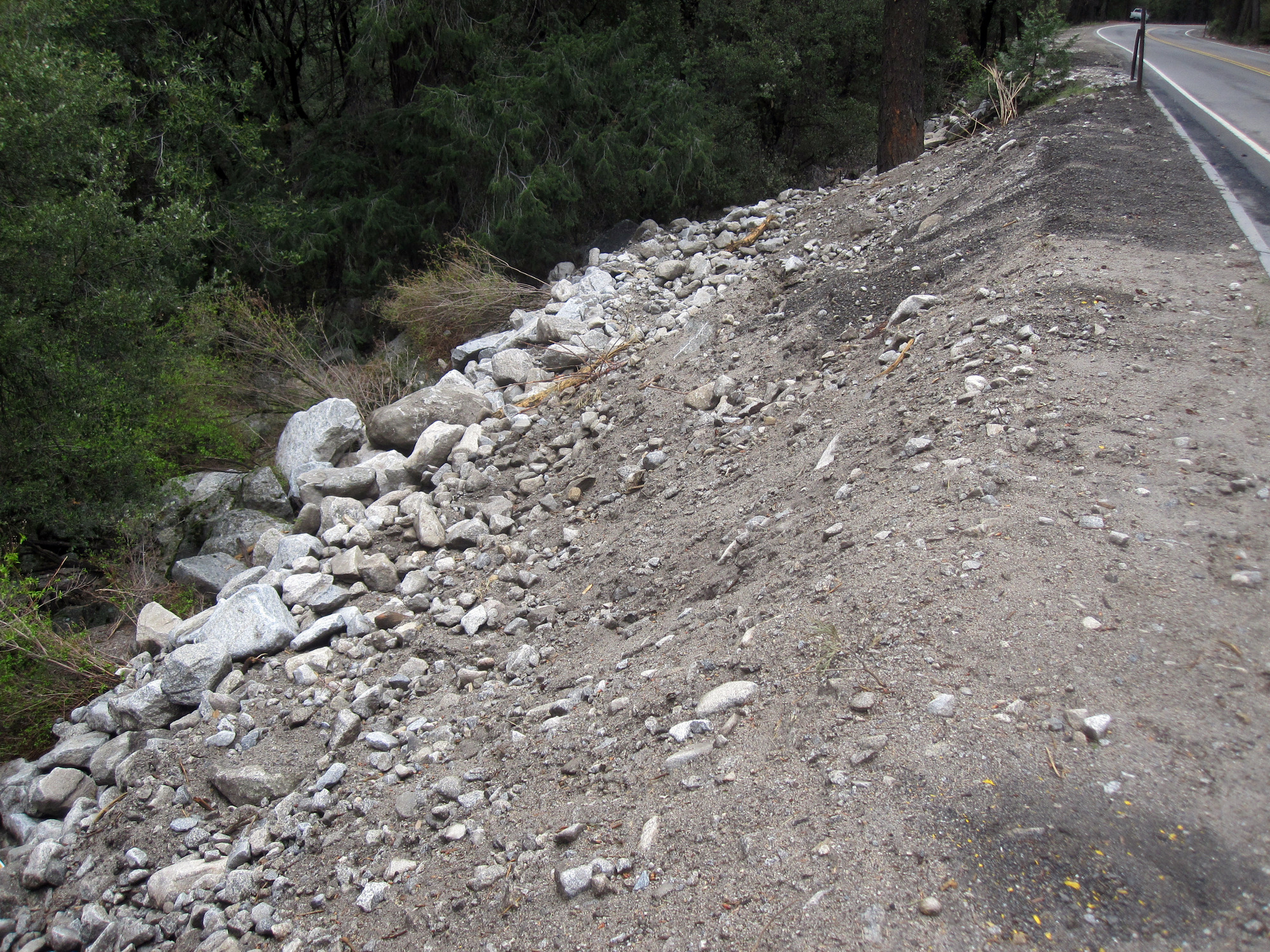 Boulders, gravel, soil, and broken vegetation pushed off into a drainage ditch to the side of the road.