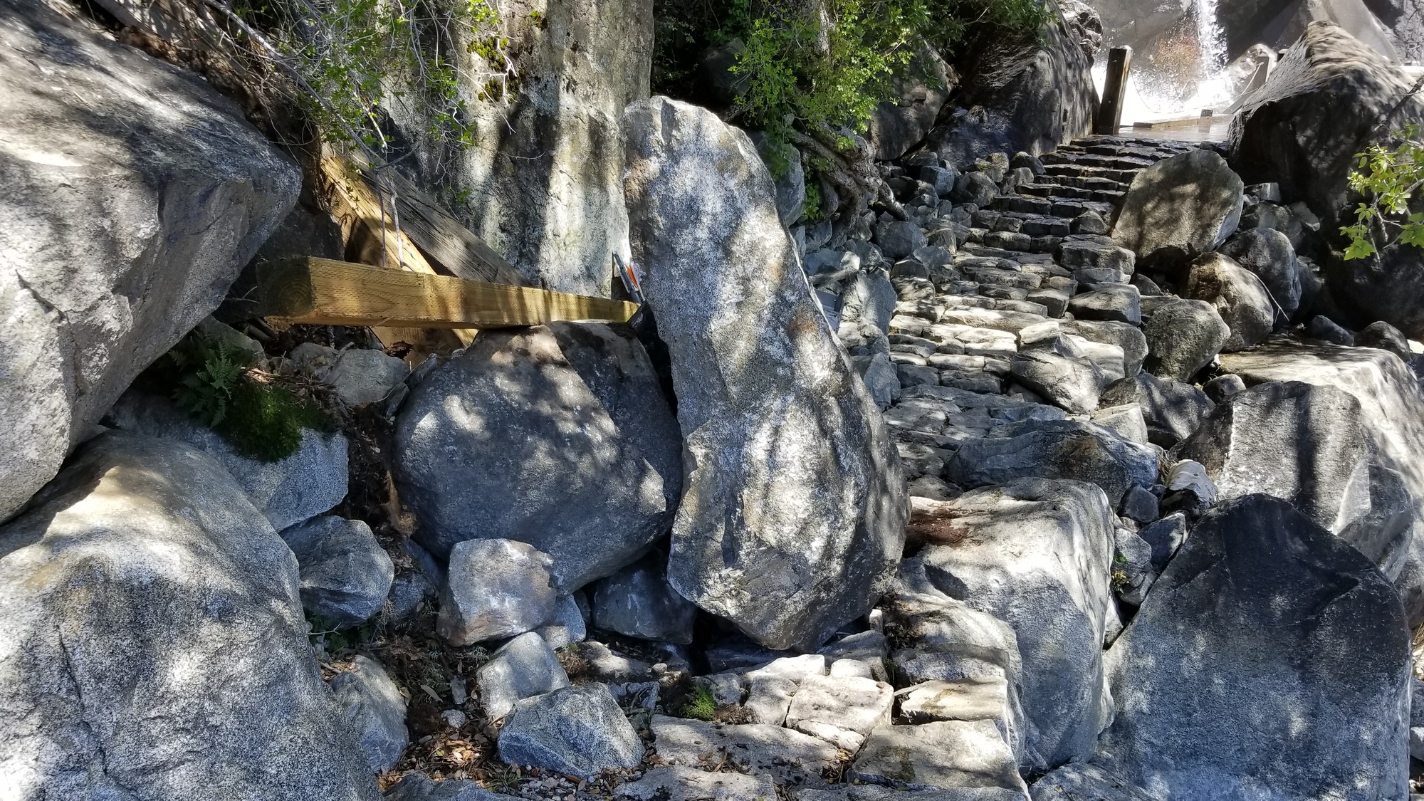 Fresh boulders resting on lumber and bridge-repair materials and partially blocking a trail.