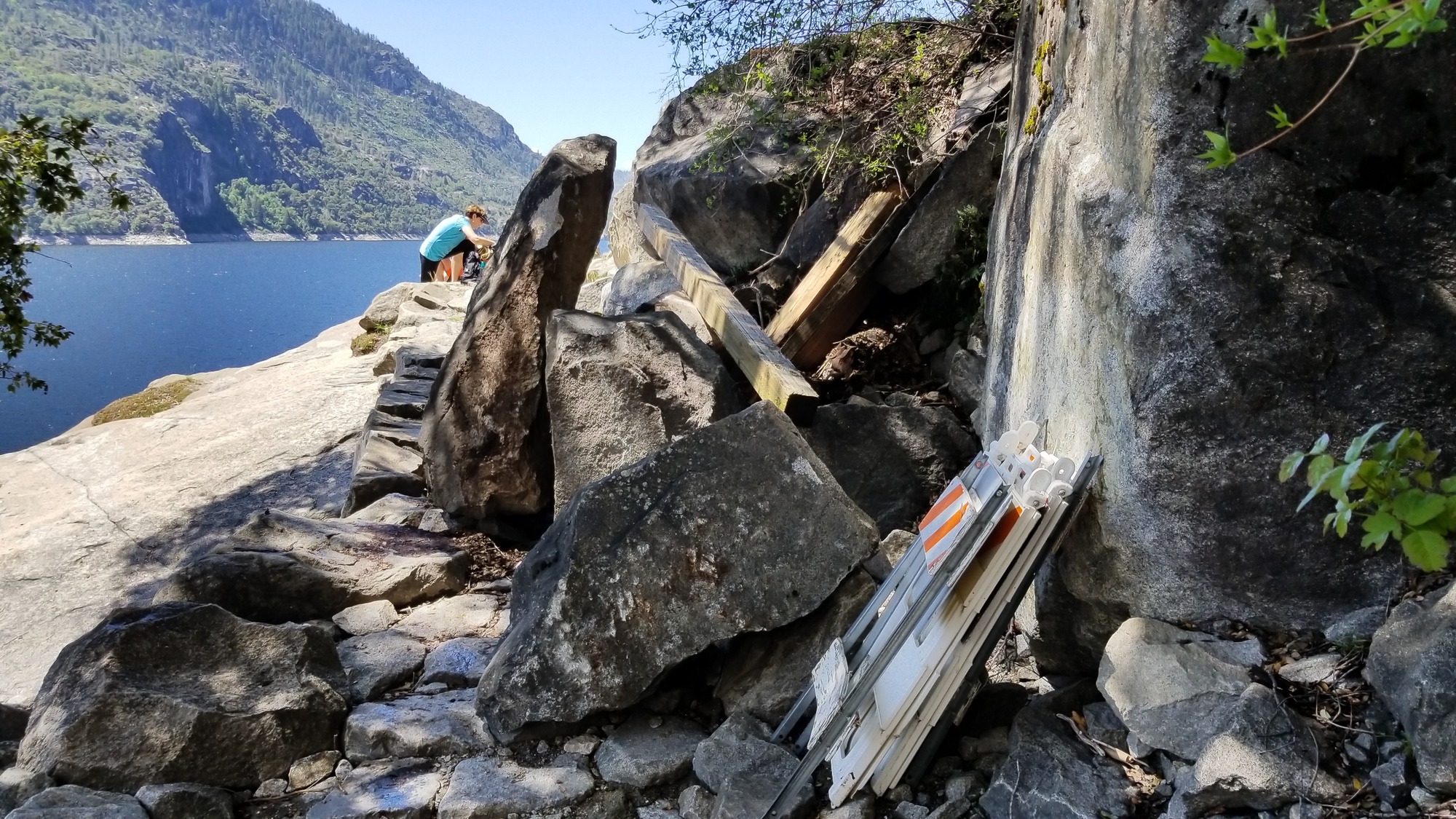 Fresh boulders resting on lumber and bridge-repair materials and partially blocking a trail.