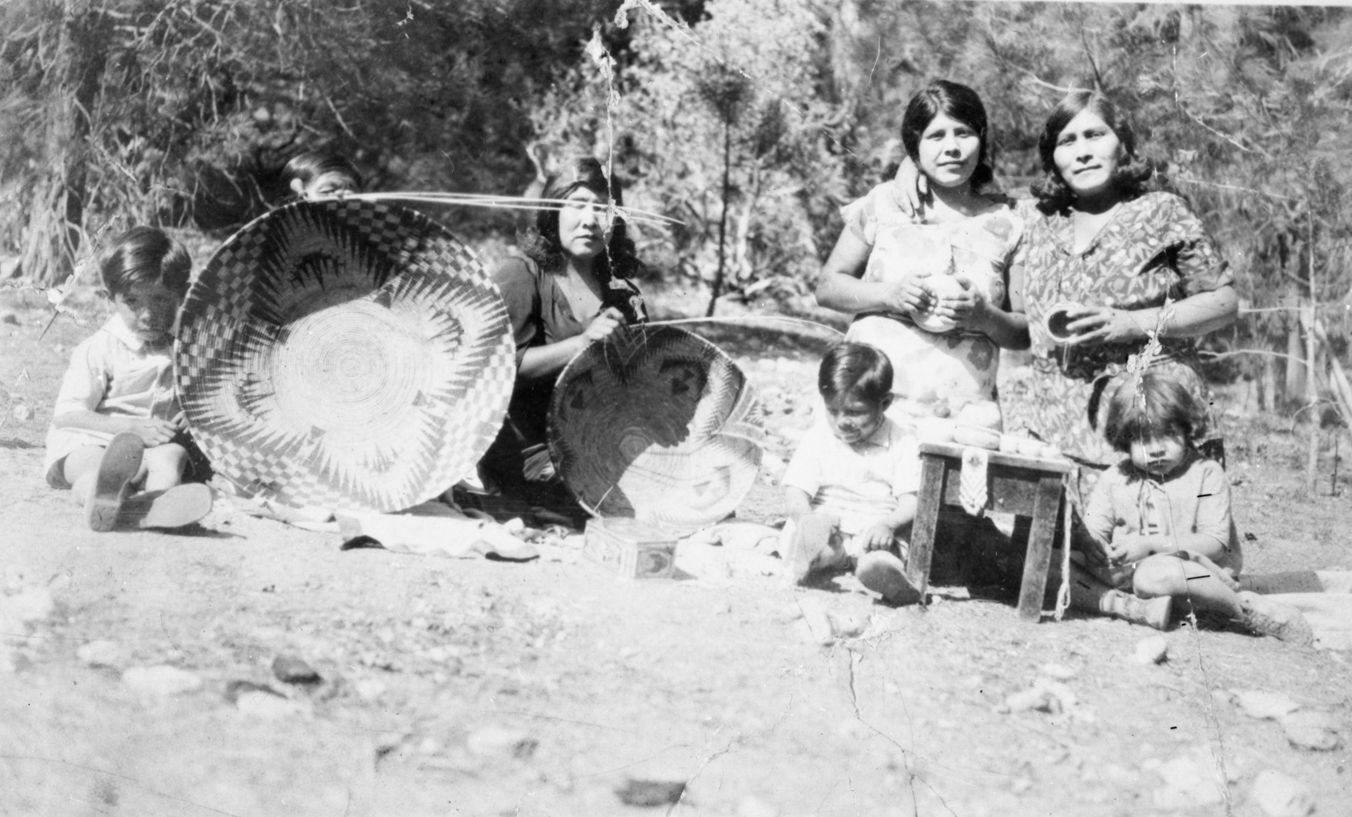 Lucy Telles and Alison Wilson weaving. Virginia Murphy (Parker) and Sarah Tom to the right holding small baskets. Clarence Parker (boy on far left) and Kenneth Parker (boy in front of Virginia Murphy Parker)