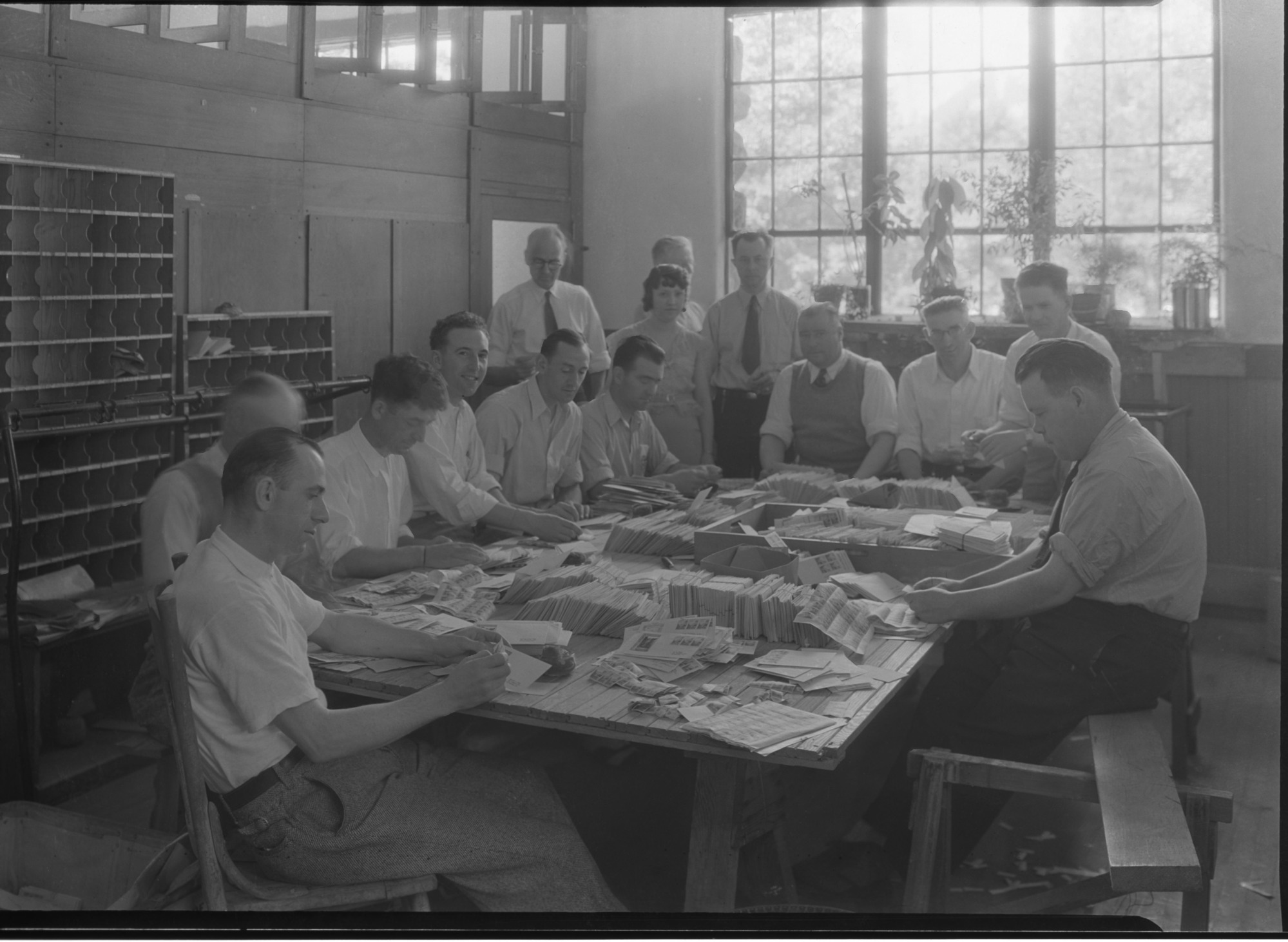 Postal Clerks at Yosemite Post Office for stamp issue 1st of the Nat. Park stamp series-the Yosemite 1 cent stamp. Distinguishable in the background are (standing up from left to right): Postmaster F.C. Alexander (dark rimmed glasses) and Robert E. Fellers, Division of Stamps Supt. (silver belt buckle). See also July, 1934 monthly Supt. reports.