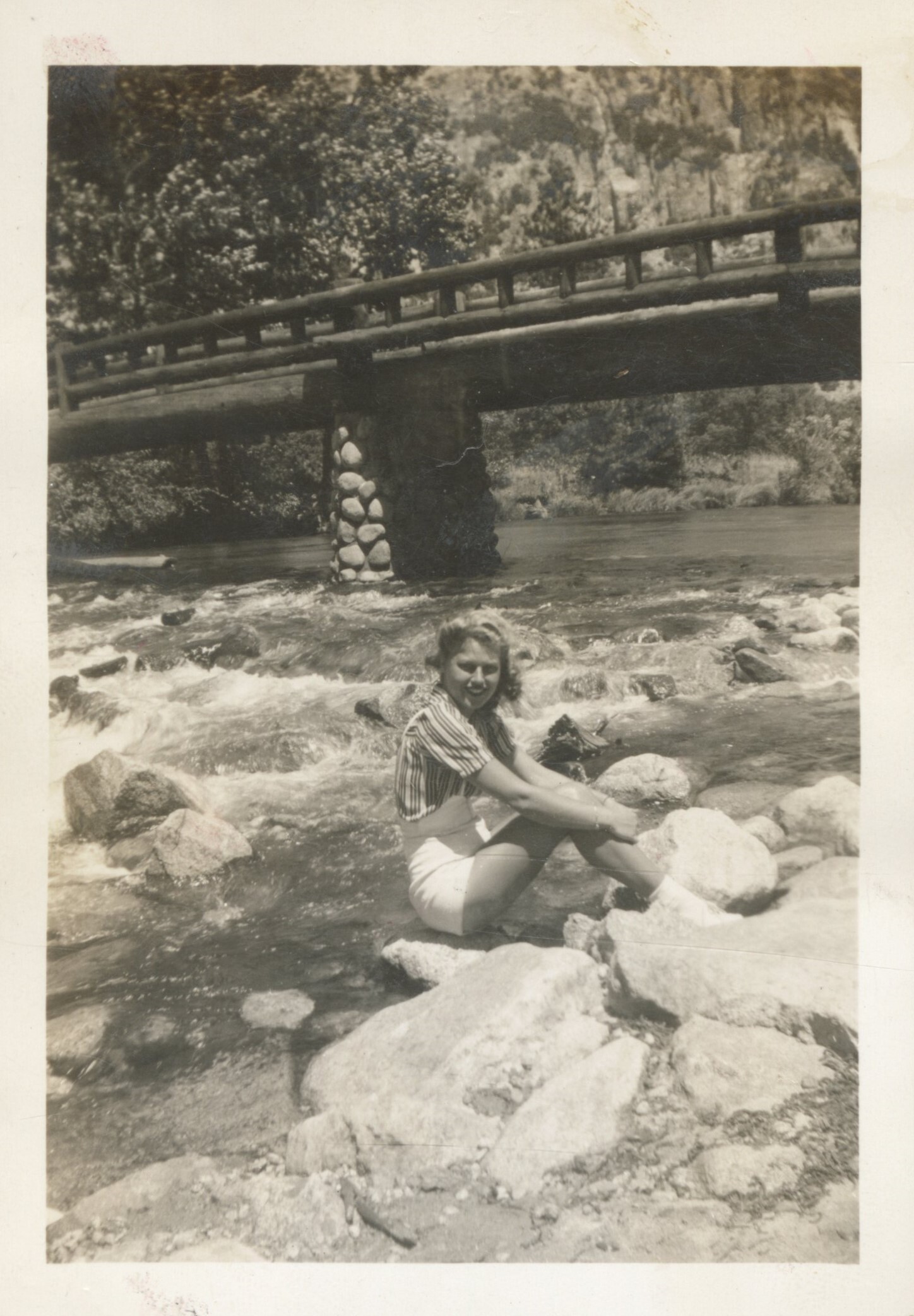 Nurse sits on a rock in the river with Housekeeping Bridge in the background