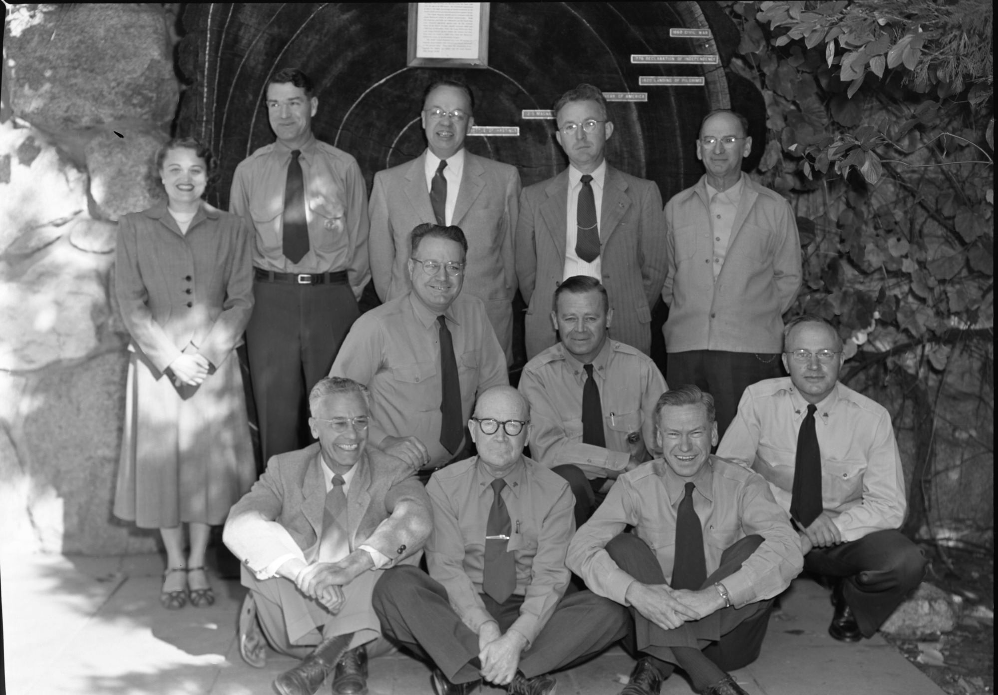 Supt. Russell and staff in front of Yosemite Museum after last staff meeting. LEFT TO RIGHT: Standing: Betty Koubelle, Homer Robinson, Carl Russell, E.C. Smith, Will Ellis. Kneeling: Emil Ernst, Duane Jacobs. Seated: Chas. F. Hill, Donald E. McHenry, Harthon L. Bill and Ralph H. Anderson.
