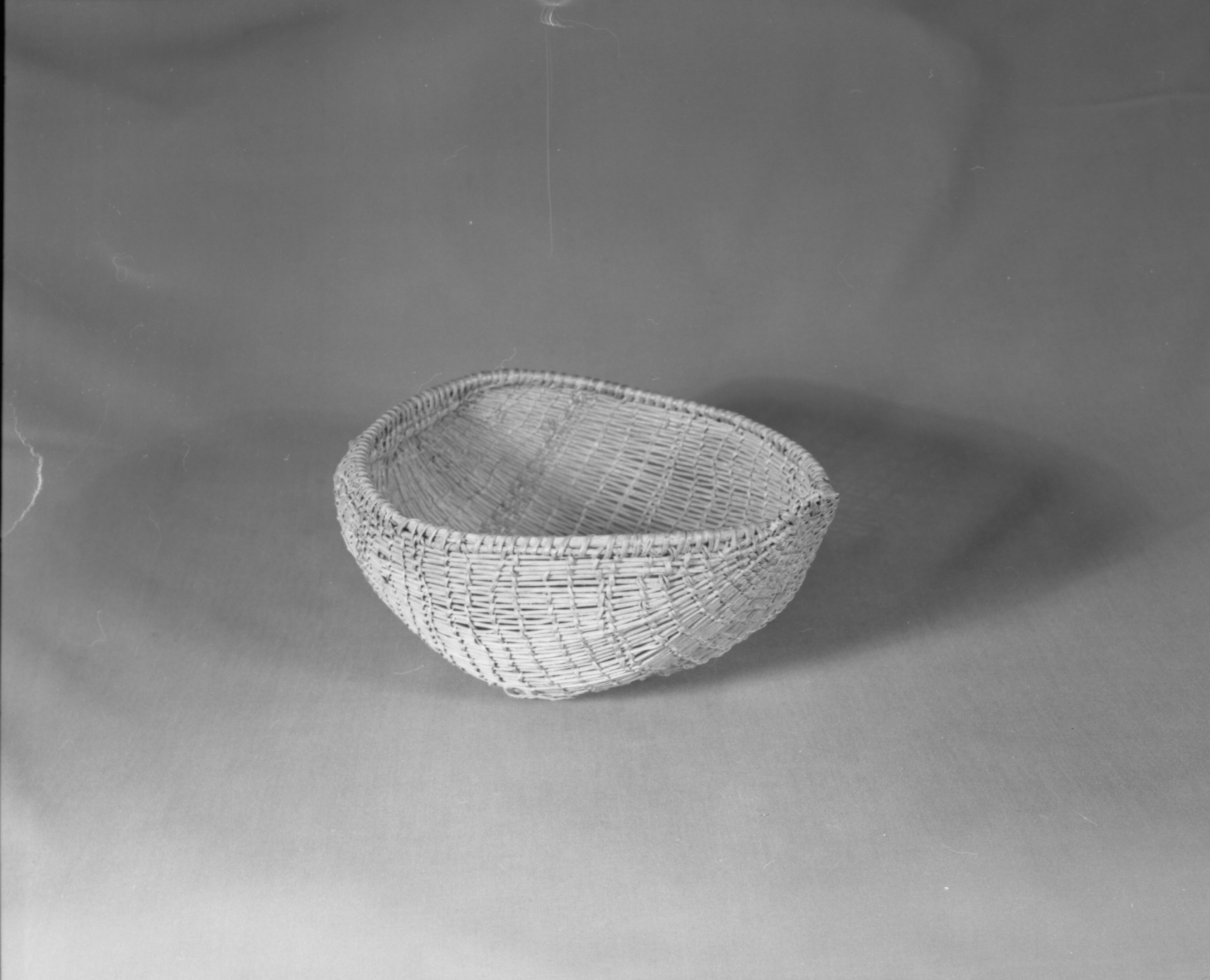 Private Collection. Object: Miwok basket. Dimensions: 9 1/2 x 4 1/2 x 8". Materials: Scraped shoots, split shoots, bracken fern root, and cotton string. Technology: Diagonally twined, up to right slant of turns, alternate rows with alternate slant. 1/3 of way from start of basket end selvage warp rods bent & lashed with additional bundle of rods coiled on top to even out rim contour. Rimstick attached with the aid of an awl lapping on one side. Repair in commericial cotton cordage apparently using a needle which secures short sections of willow sticks much in the manner of Anglo sock darning. Collection History: Purchased at 3 Flags Trading Post, Coleville, CA. with Miwok identification. Catalogued by Craig Bates and Barbara Beroza. Yosemite Collections, National Park Service.