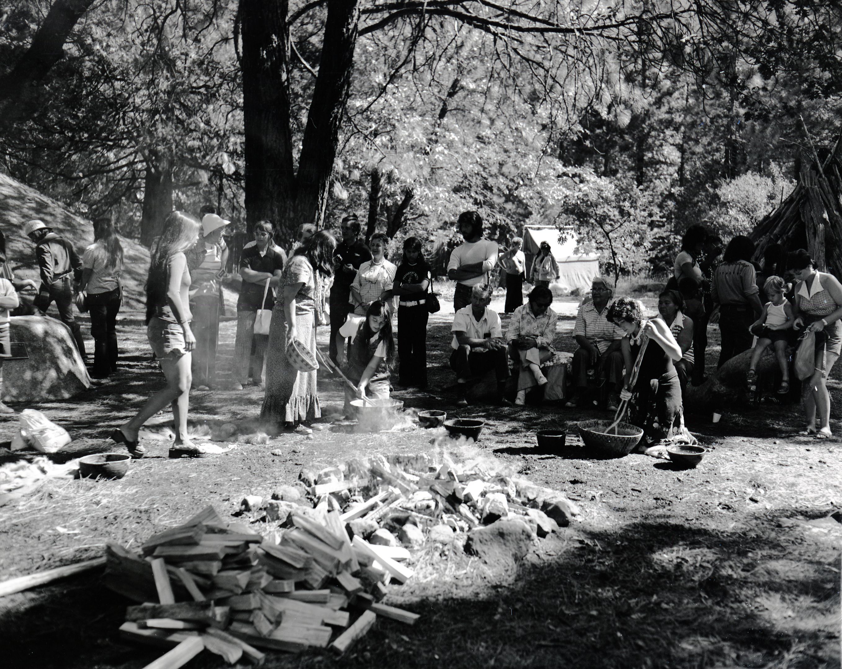 Cooking acorn mush at the Roundhouse Dedication, Yosemite Valley. Julia Parker, standing with basket in hand. Felicia Espina, (left) and Kim Hamilton (right) cooking in basket.