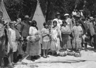 Showing baskets. Man in white cap is James Schwabacher & Forrest Townsley is next to him. Walter Starr Sr. on Schwabacher's left. Front Row L-R: Tina Charlie, Carrie Bethel, Alice Tom James Wilson, Leanna Tom & Maggie Howard.