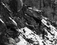 Man standing beneath halfpipe culvert on steep slope, snow on ground.