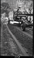 Worker driving a road grader in Zion Canyon. Labeled 'experimental road paving. Processing sand and bitumul 60'.