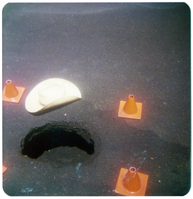 Pothole in need of repair surrounding by orange traffic cones.