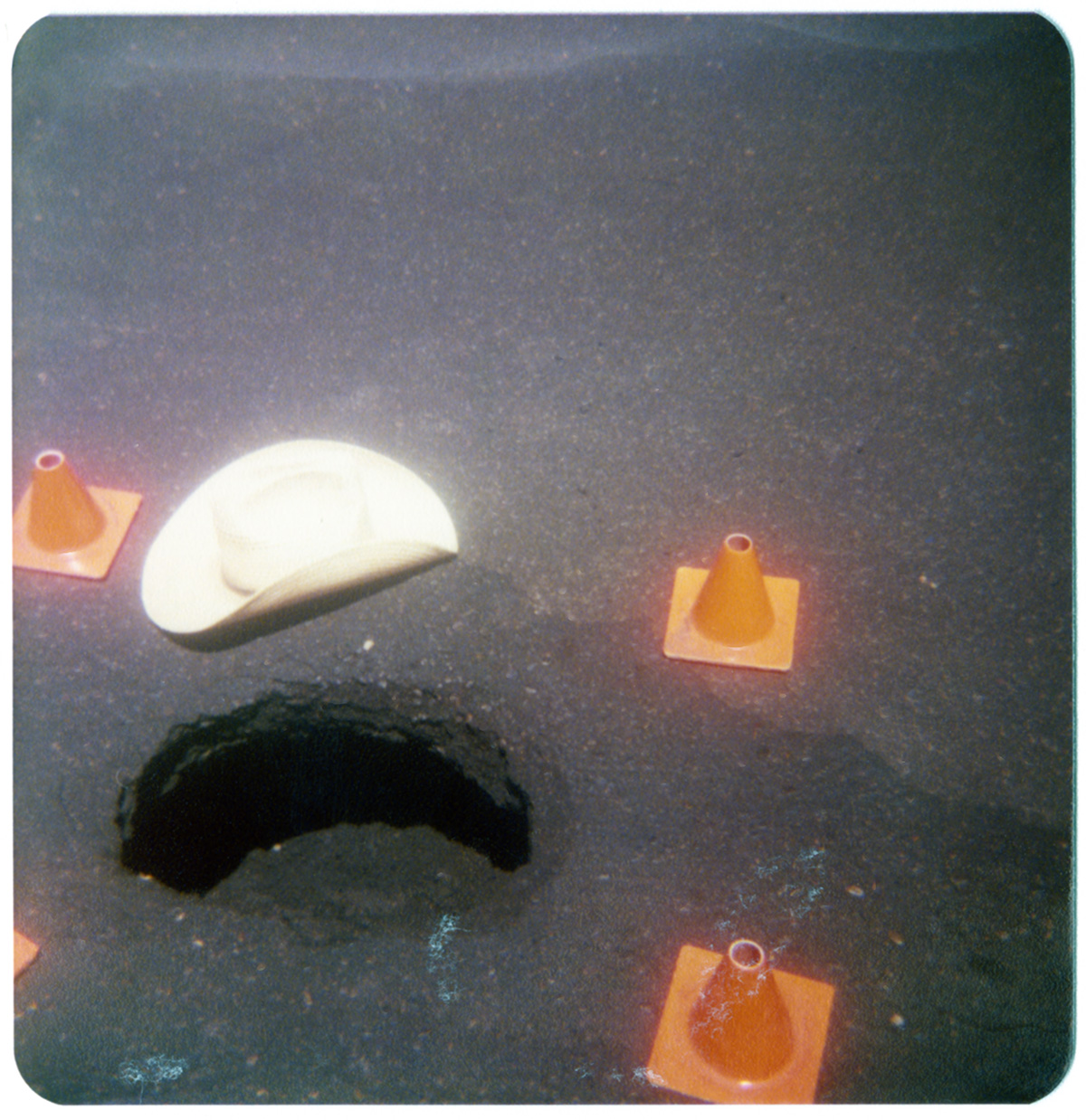 Pothole in need of repair surrounding by orange traffic cones.