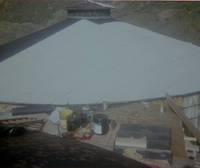 Water tank with new roof in progress, supplies for reroofing project set on scaffold in foreground.