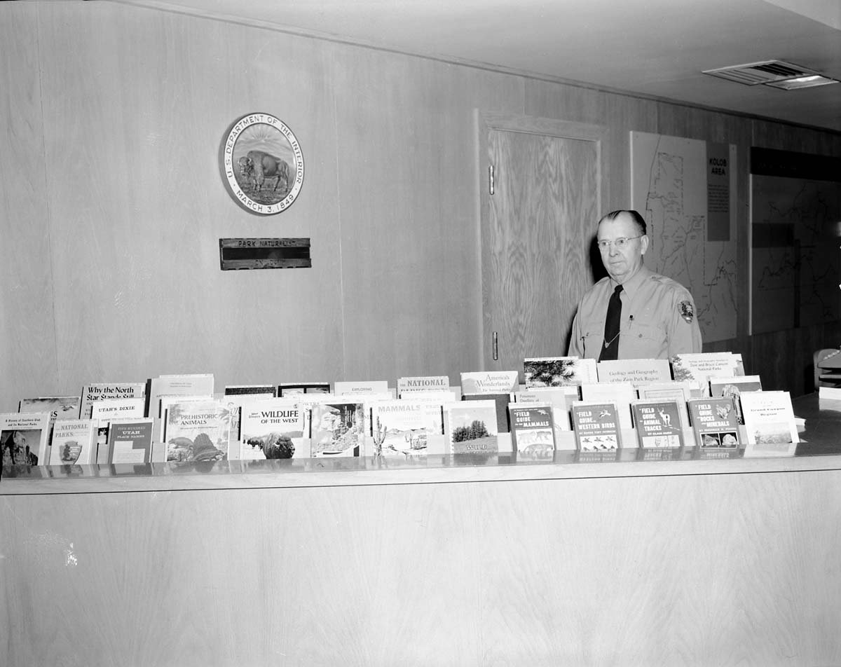 New display area for Zion Natural History Association and other sales publications at Visitor Center information desk- Chief Naturalist Carl E. Jepson in photo.