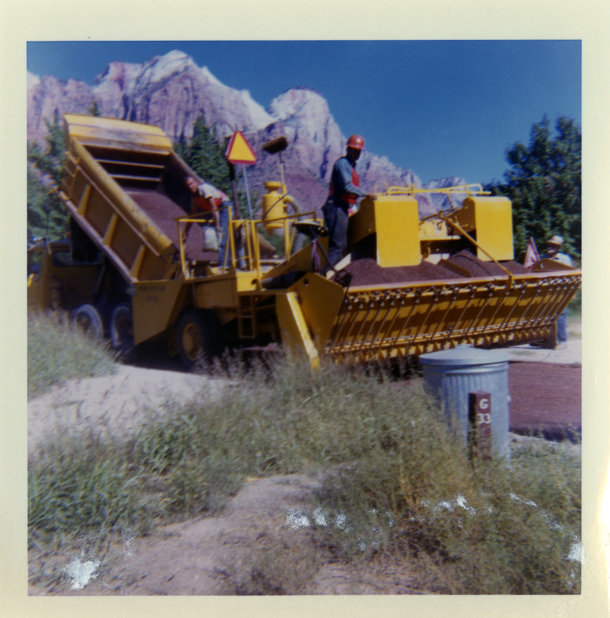 Men operating dump truck and chipsealing machine to chipseal roads.