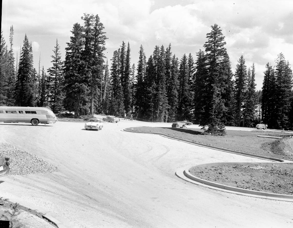 Cars and visitors in the partially constructed parking area at Point Supreme. Utah Parks Company bus parked at left, construction equipment at right. View back towards museum.