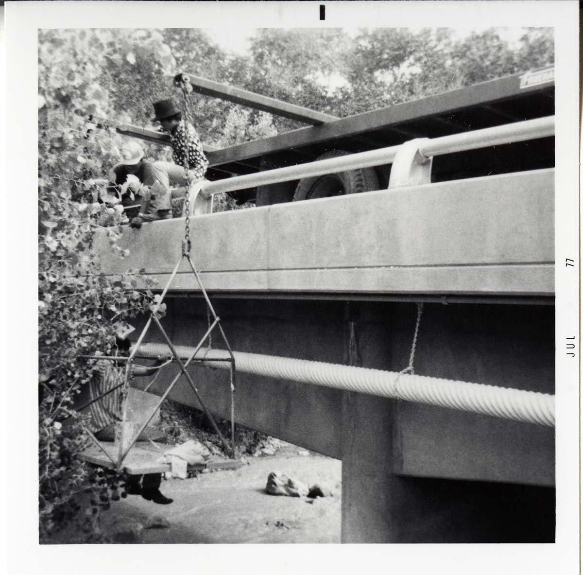 Workers place pipe on side of bridge during the Watchman housing utility project.