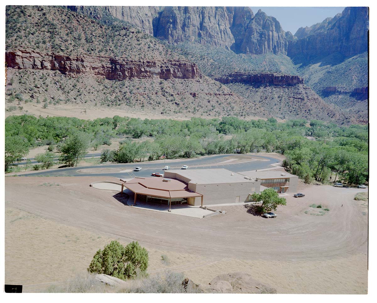 The old visitor's center and headquarters building and surrounding dirt lot, view south.