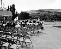 National Park Service Midwest Regional Director J. Leonard Volz addressing visitors at the dedication of new Tribal and National Park Service Visitor Center and 50th anniversary at Pipe Spring National Monument. United States and Department of the Interior flags at either side of grandstand.