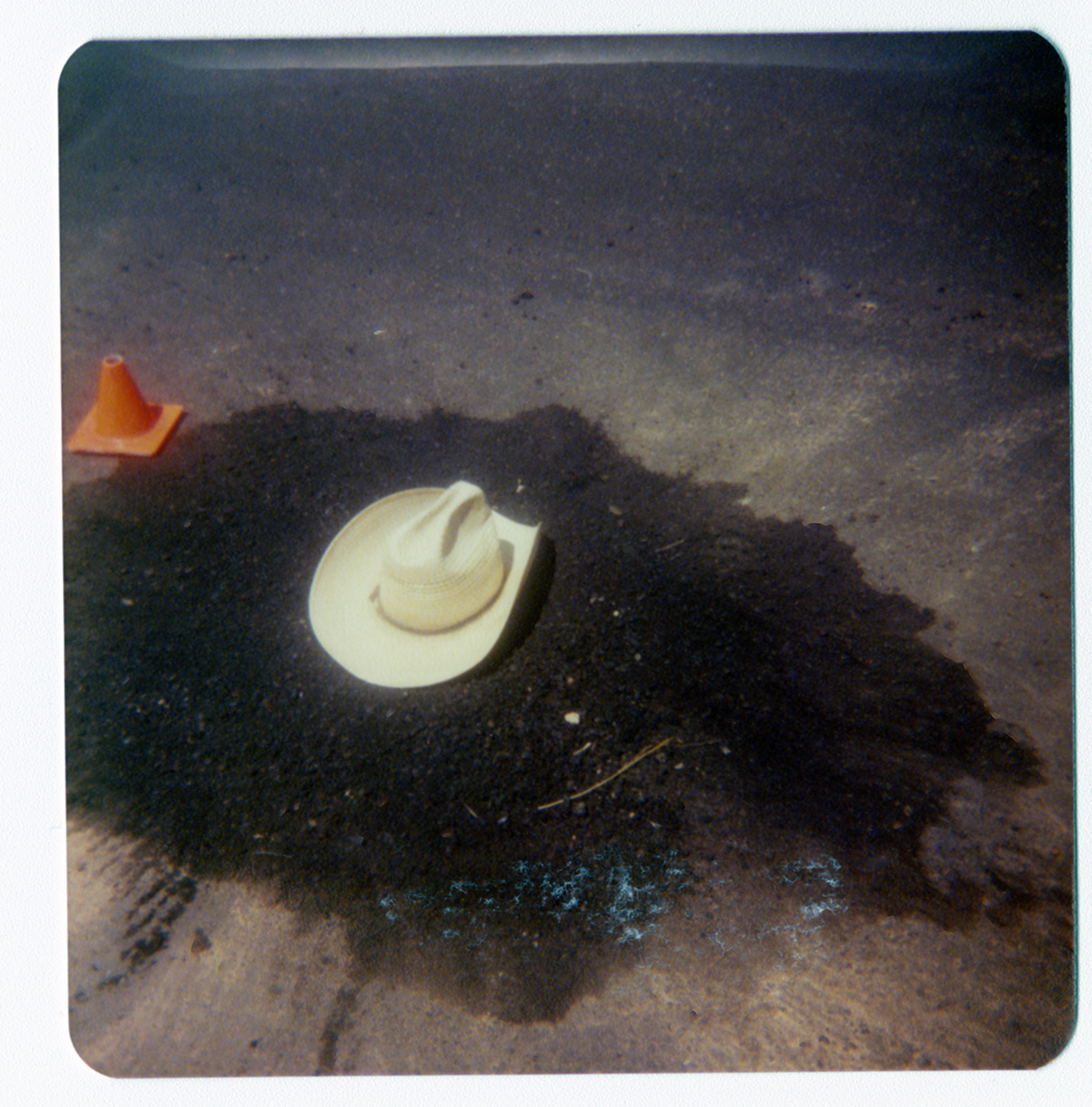 New sealcoat covering pothole with workers hat resting on top.