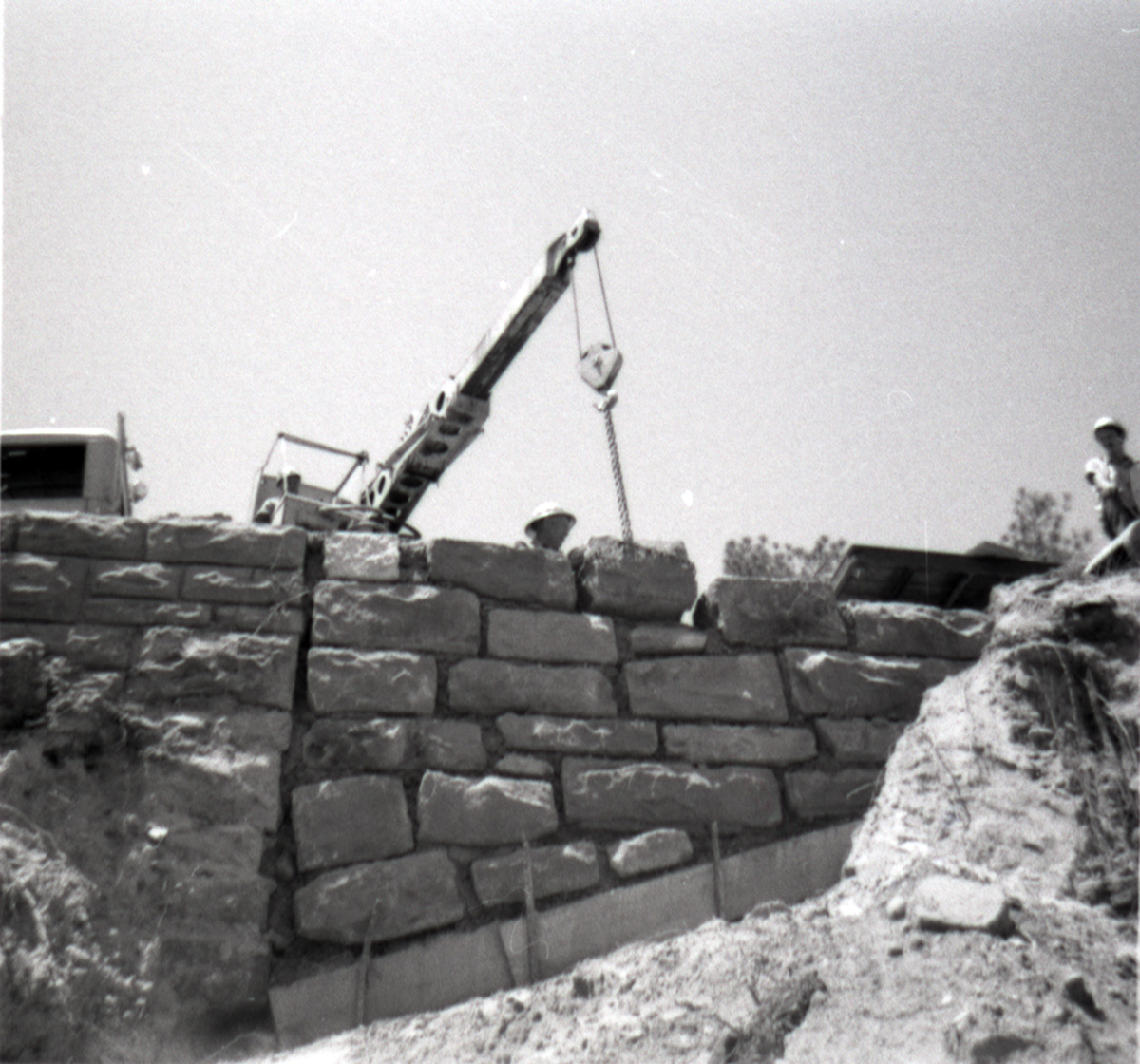 Men operating crane to place rocks for retaining wall along East Rim road during repairs.