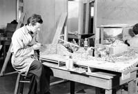 Civilian Conservation Corps (CCC) worker constructing miniature stone wall for the Zion Pueblo diorama, diorama shows Pueblo figurines building structures.