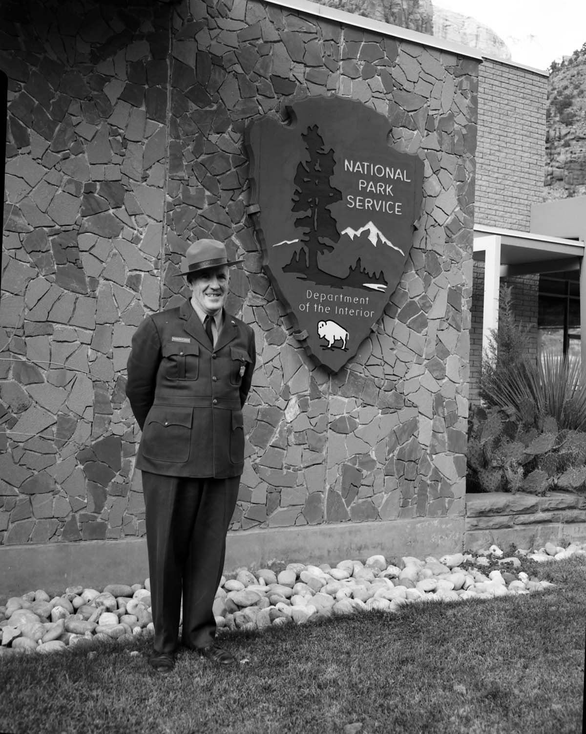 Rudy Lueck at time of retirement, next to NPS arrowhead outside Mission 66 Visitor Center and Museum and headquarters.