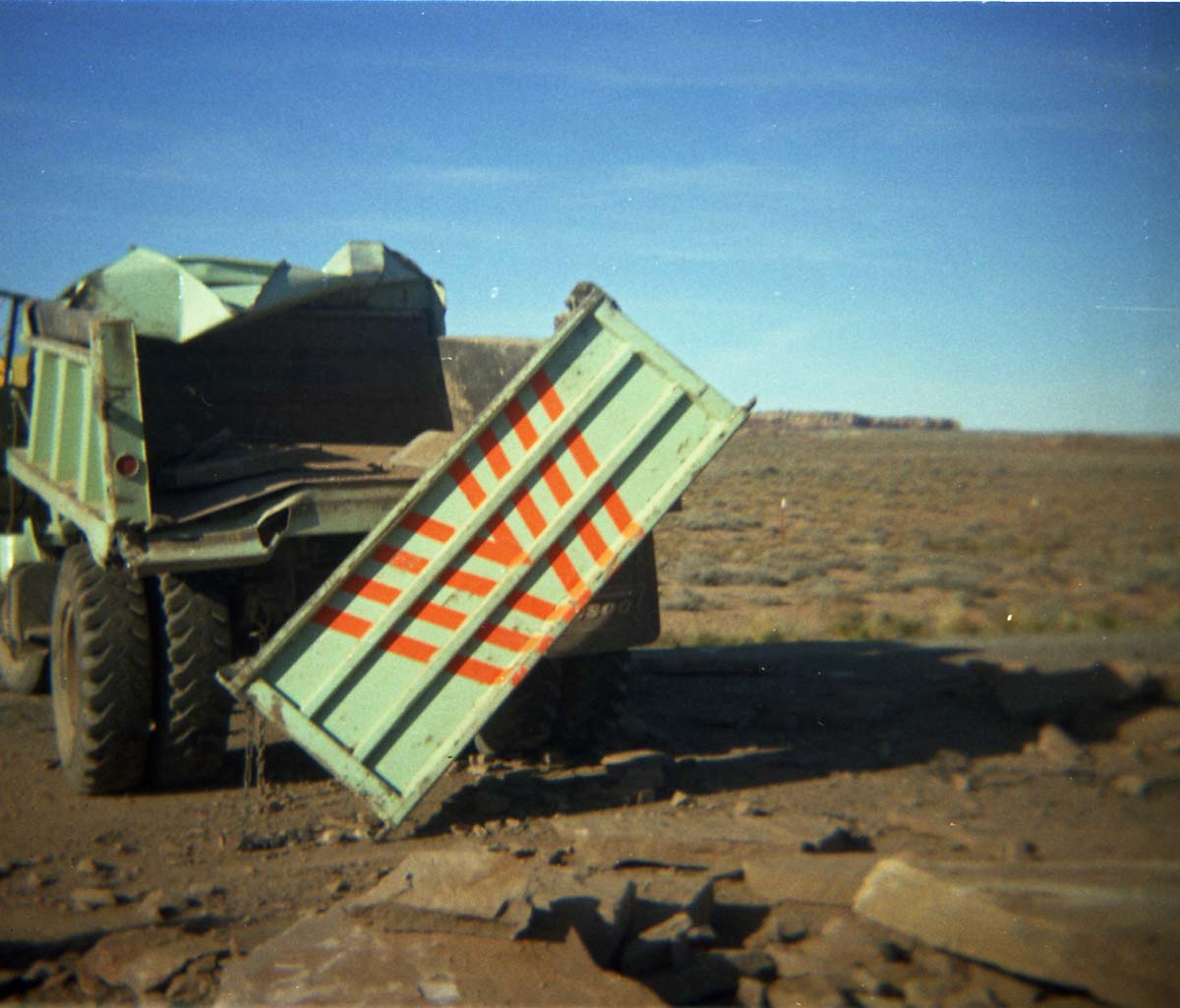 Color Photo of a damaged dump truck- tailgate and side ripped open.
