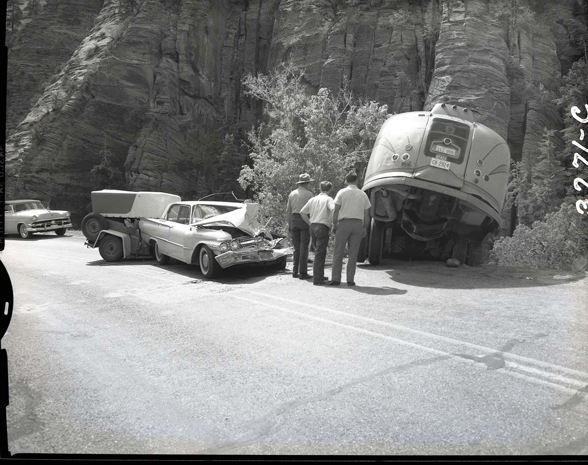 Collision between private car (Ford) towing U-Haul trailer and (Utah Parks Company) bus. View of car and bus - car apparently on wrong side of road.