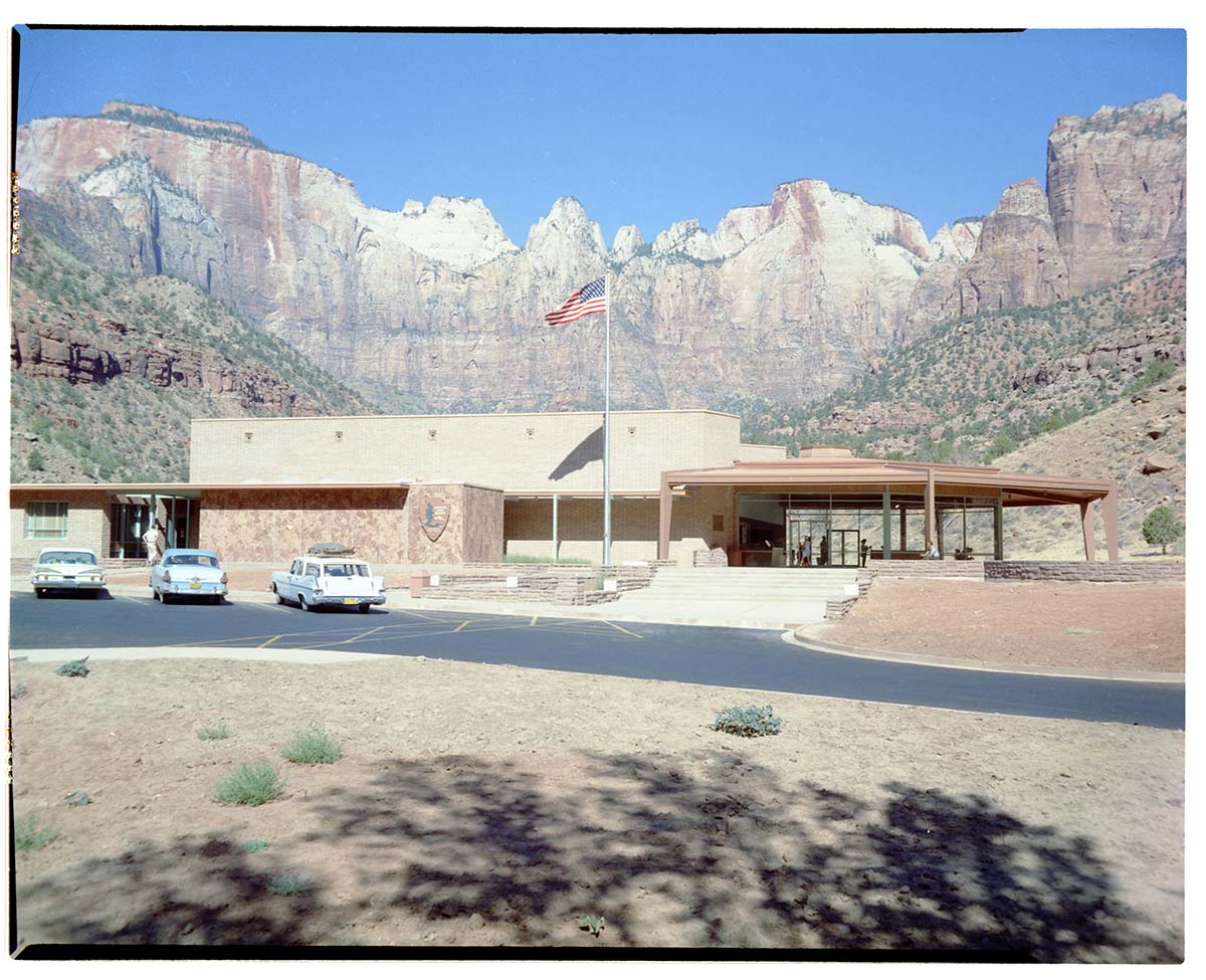 Headquarters building with vehicles parked in the parking lot and a backdrop of The Altar of Sacrifice, Sundial, and West Temple.