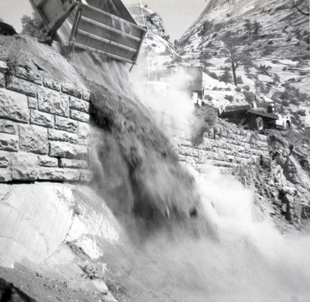 Dump truck dumping dirt during retaining wall repairs along East Rim road.