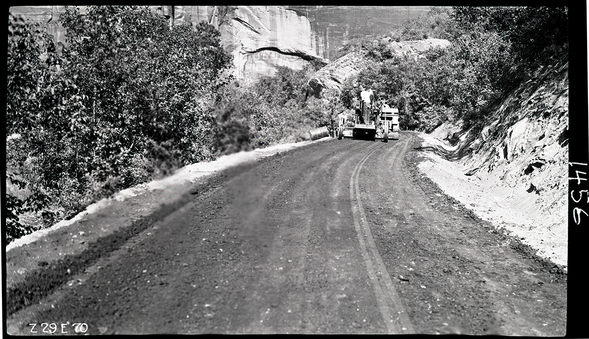 Workers engaged in experimental road paving of the floor of the valley road, smoothing the processed material to ready it for compaction.