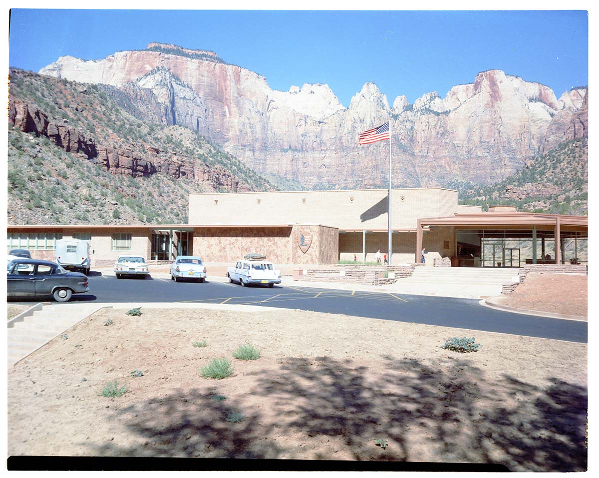 Headquarters building with vehicles parked in the parking lot and a backdrop of The Altar of Sacrifice, Sundial, and West Temple.