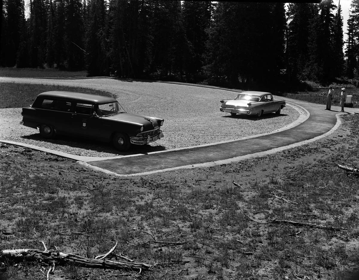 Man and woman stand near car parked in the newly constructed parking area at Chessman Ridge Overlook. National Park Service station wagon parked at left. Taken as a record of completed project. [No positive for this negative]