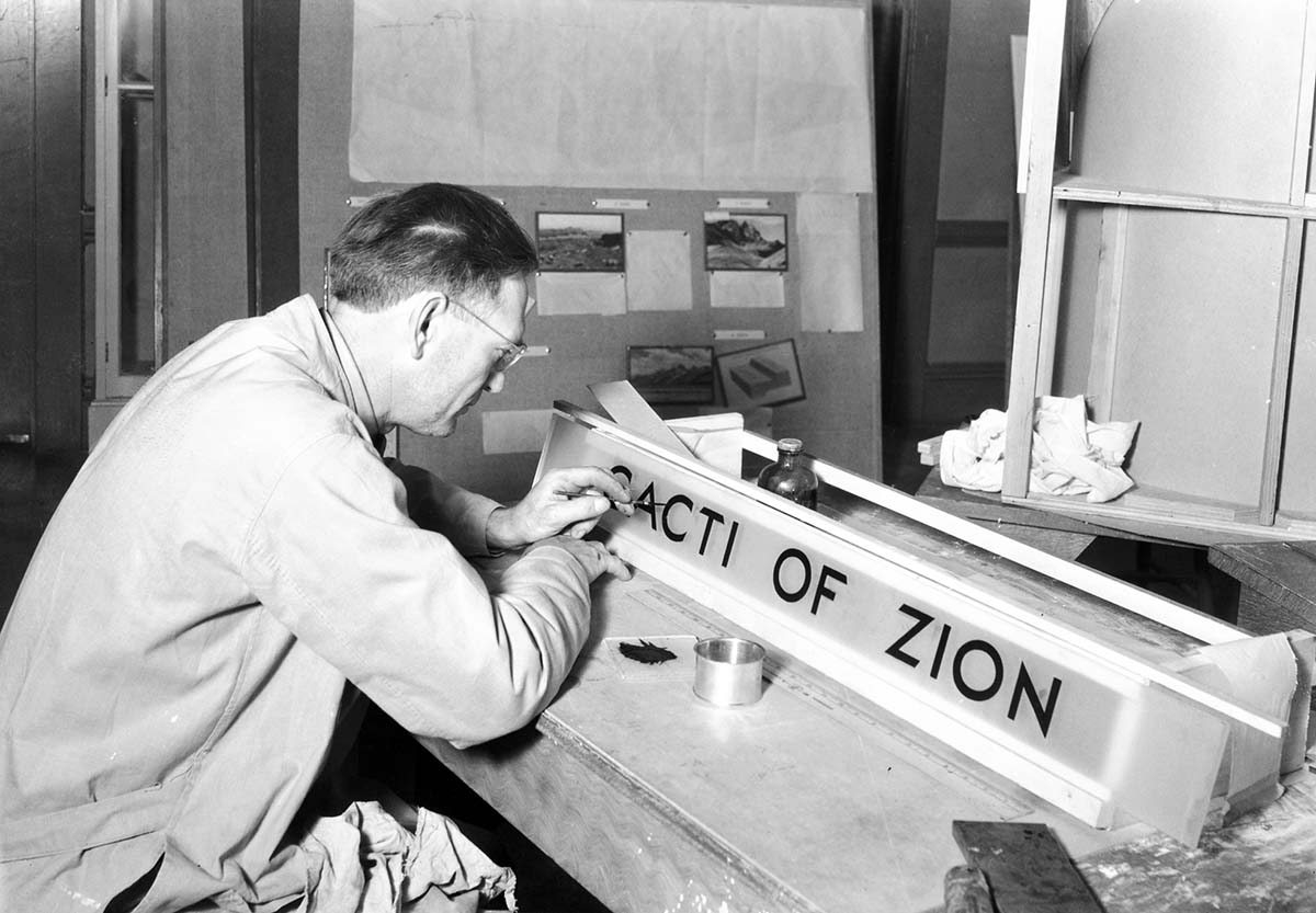 Western Museum Laboratory (WML) worker painting a sign 'the cacti of Zion' for the Zion Museum's cactus diorama exhibit.