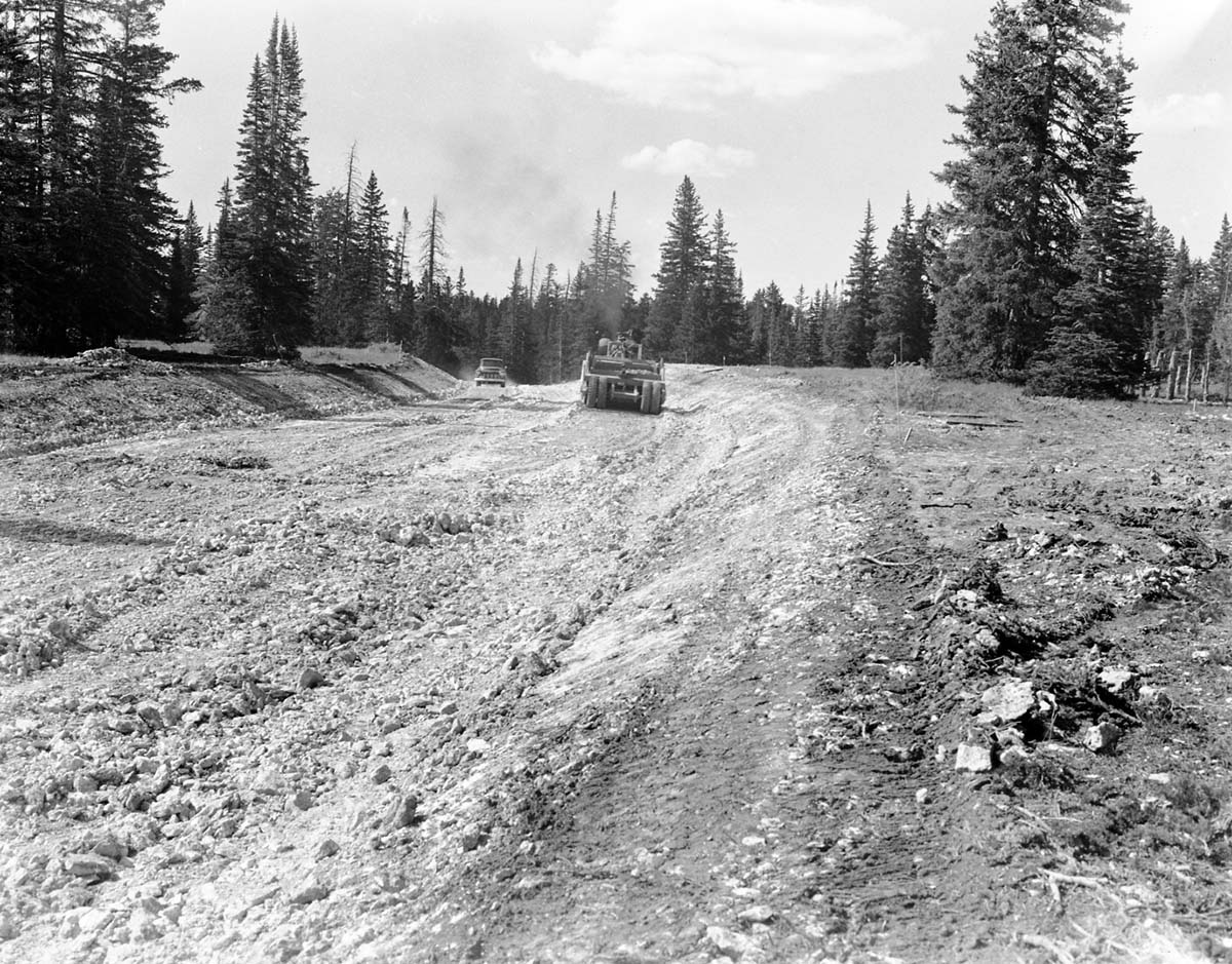 Bulldozer working on rim road construction, with pickup truck driving on new road grade.