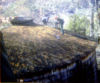 Two men removing shingles from water tank during reroofing project.