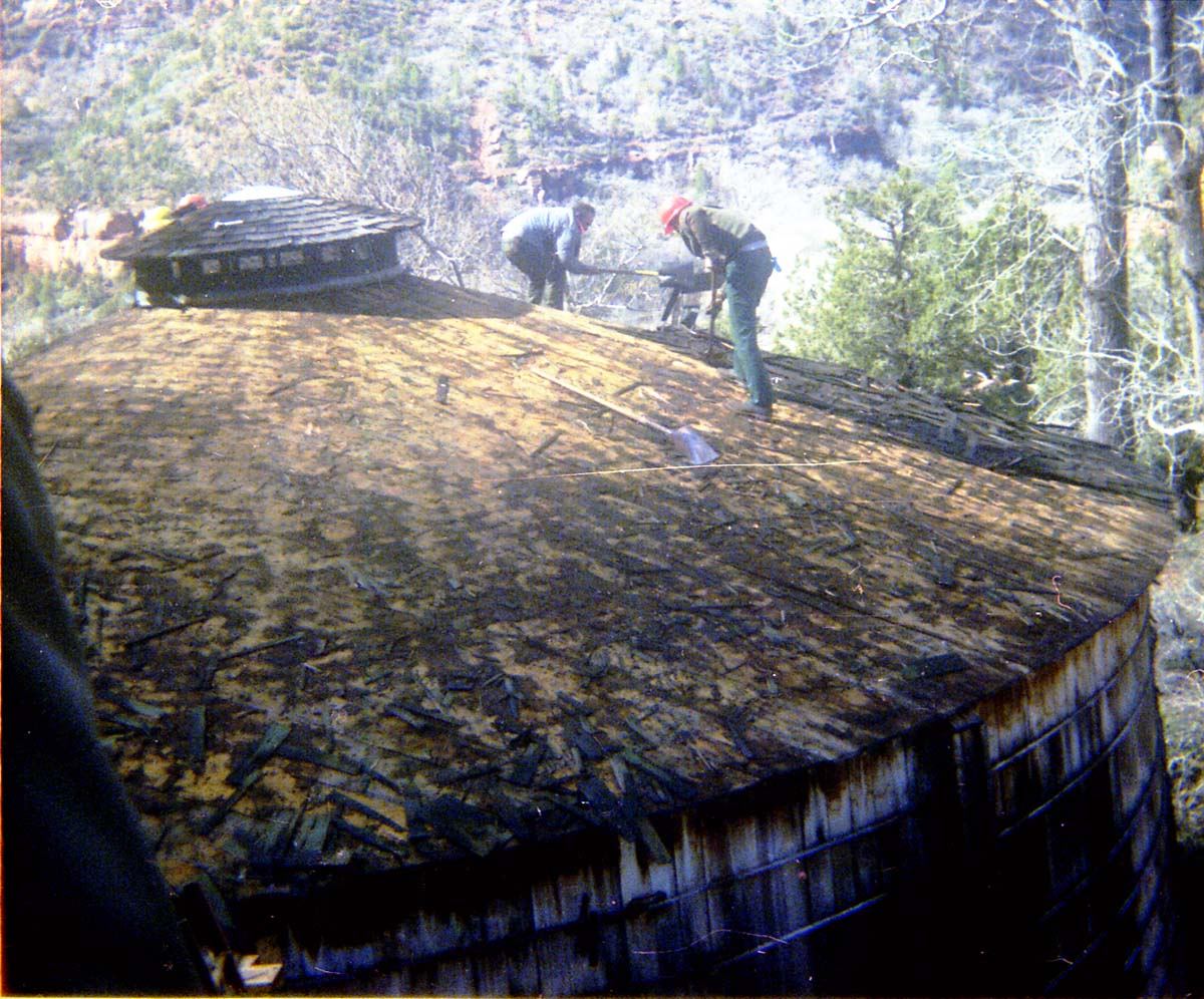Two men removing shingles from water tank during reroofing project.