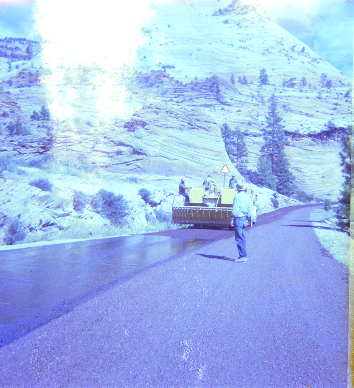 Men performing road construction with Zion landscape in background.