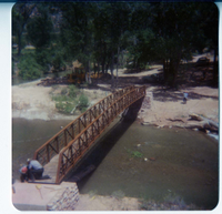 Two men working on the new Grotto footbridge across the Virgin River, equipment in background. Before trail created to access bridge.
